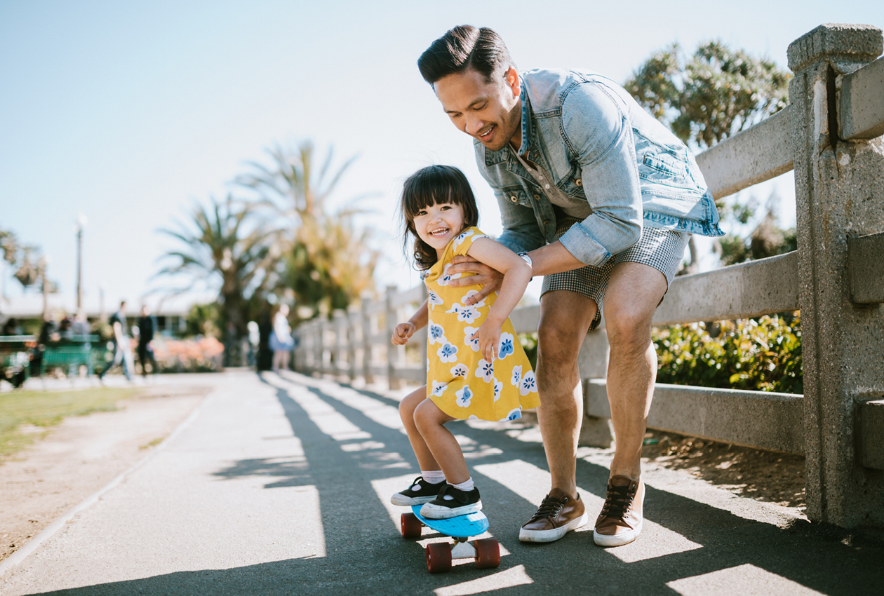 Father pushing daughter on skateboard
